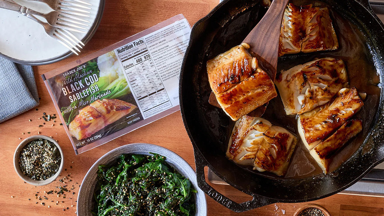 A cast iron skillet with braised cod next to a package of Trader Joe's Wild Alaskan Black Cod Sablefish with Miso Marinade