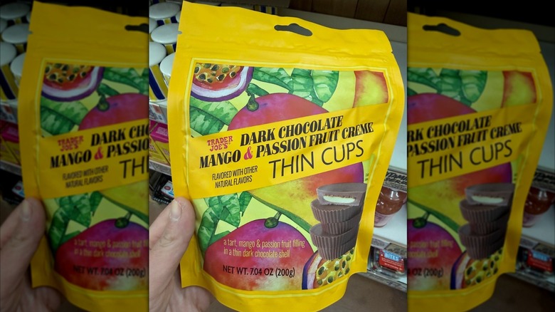 A person holding a package of Trader Joe's Dark Chocolate Mango & Passion Fruit Creme Thin Cups