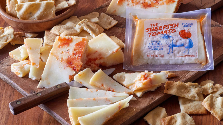 A block of cheese sliced up on a cutting board next to a package of Trader Joe's Sheepish Tomato cheese