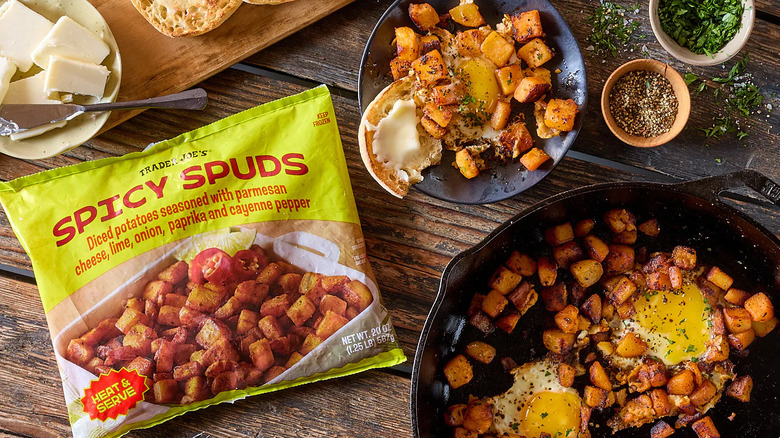 A bag of Trader Joe's Spicy Spuds on a wooden board with cooked potato and eggs in plates