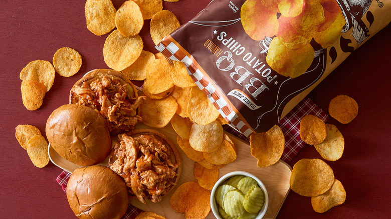 Trader Joe's BBQ Flavored Potato Chips poured out on a red surface surrounding two barbecue sandwiches
