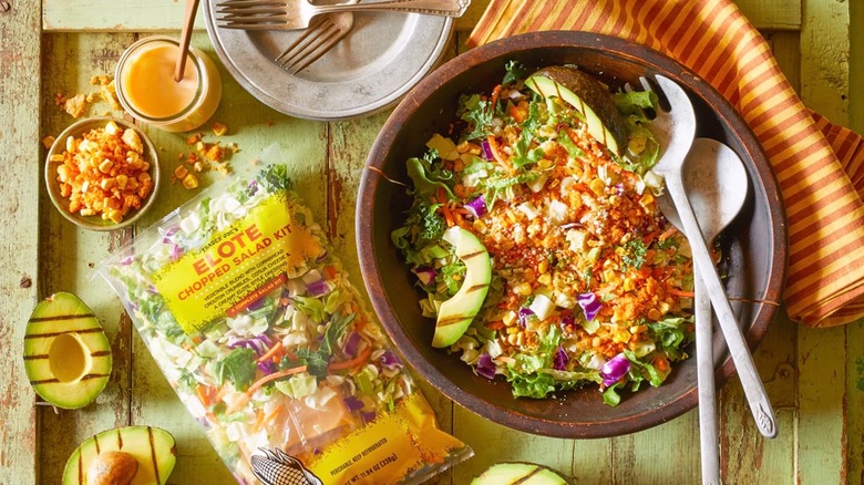 Bag of Elote Chopped Salad Kit from Trader Joe's next to large bowl of salad on green wooden surface