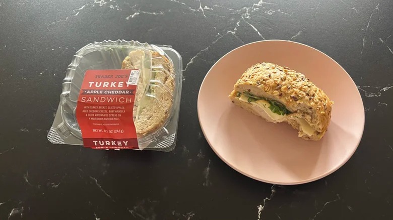 Trader Joe's Turkey Apple Cheddar Sandwich half on pink plate next to packaging on black surface