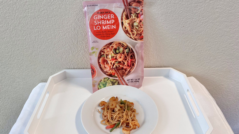 Some Trader Joe's ginger shrimp lo mein on a plate with a whole pack leaning on the wall in the back
