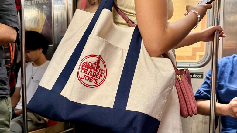 Woman on subway train holding smartphone with Trader Joe's navy and beige canvas bag over her shoulder