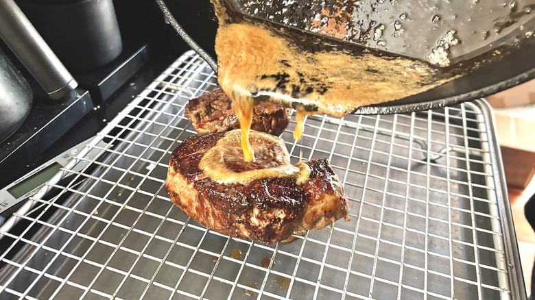 Pouring butter from cast iron skillet onto steak resting on rack