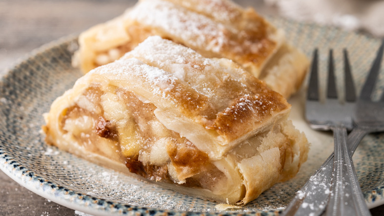 Overhead view of a sliced apple strudel on a sheet of wax paper with crumbs surrounding it
