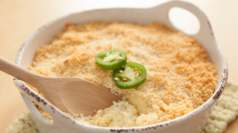 A jalapeno cheese dip in a white serving bowl with a spoon dipped in.