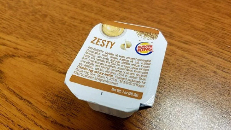 A sealed package of Burger King's zesty dipping sauce on a wooden table top