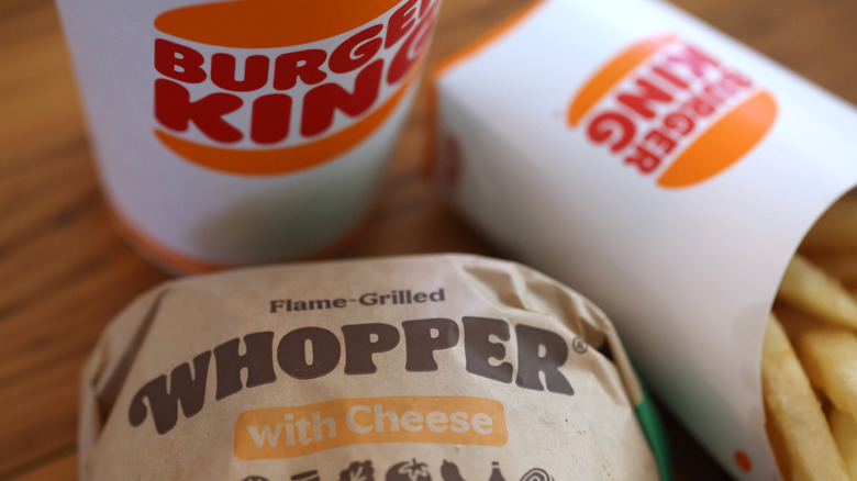 A Burger King Whopper still wrapped in paper sitting next to Burger King fries and a Burger King drink.