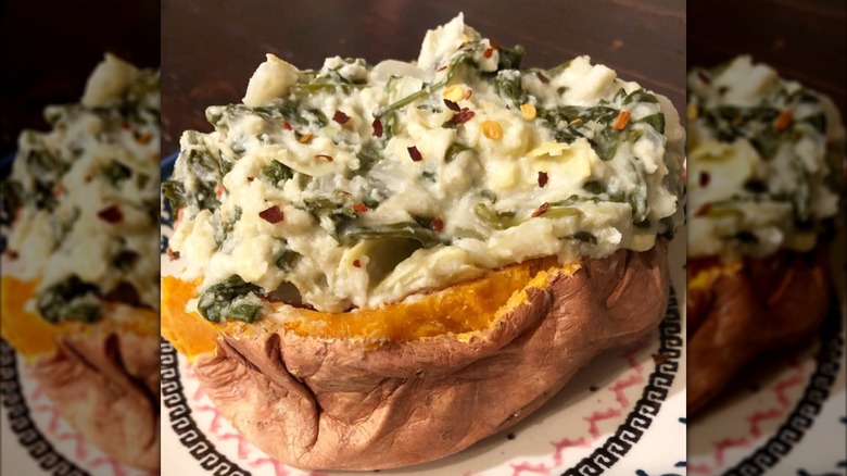 Baked potato with spinach artichoke dip on plate.