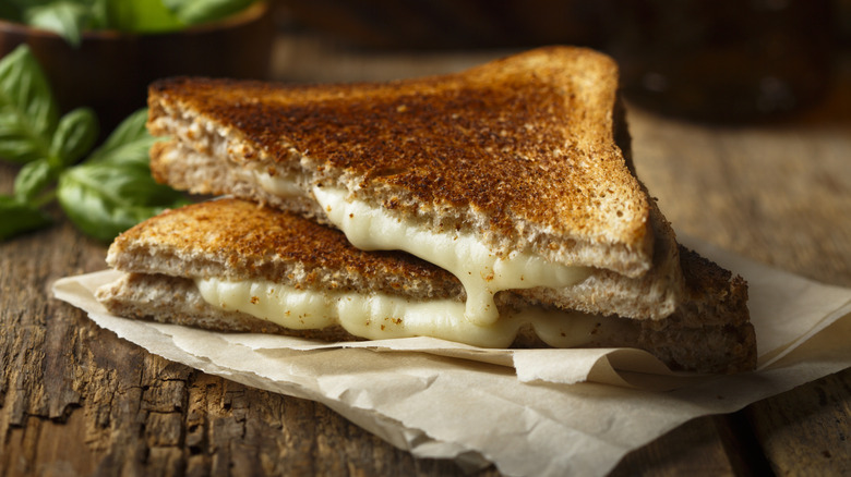 Classic grilled cheese sandwich on folded parchment paper on a wood table wit fresh basil leaves in the background.