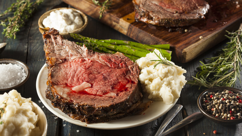 A cut of prime rib sitting on a plate with asparagus and mashed potatoes