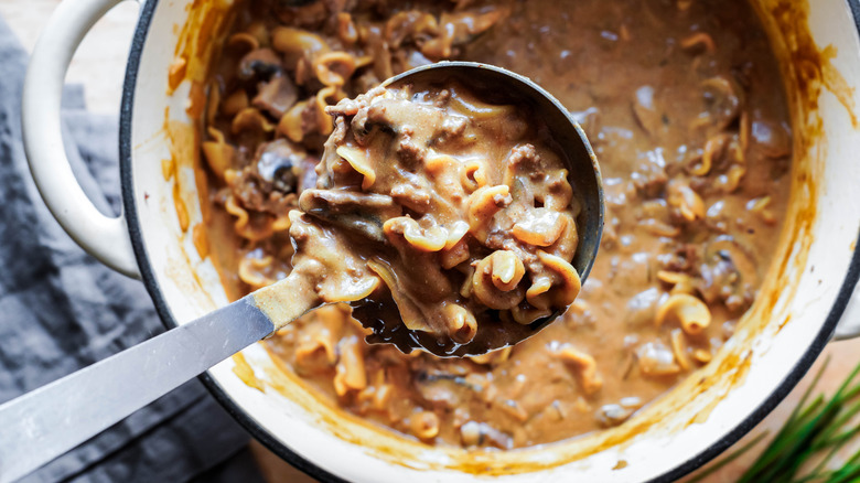 Ladle full of ground beef stroganoff above a large pot of the same