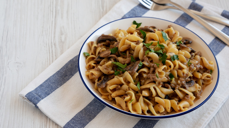 Bowl of beef stroganoff garnished with fresh herbs on a blue-striped tea towel