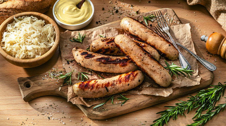 Bratwursts and sauerkraut presented on a board with mustard and rosemary