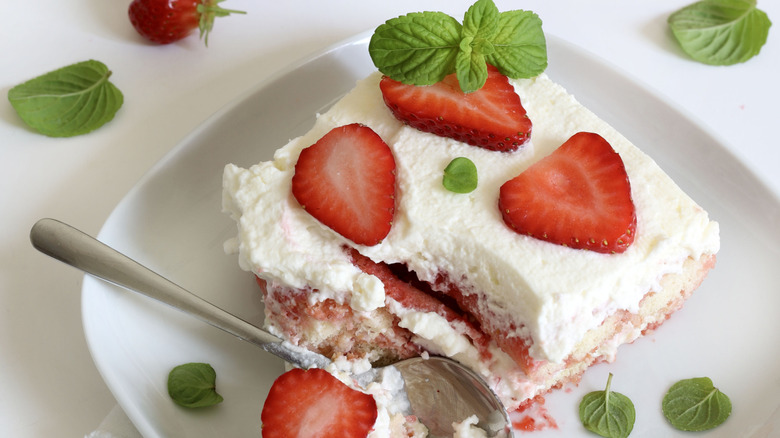 Square slice of strawberry cake with layers of strawberry filling and cream garnished with strawberry slices and mint leaves