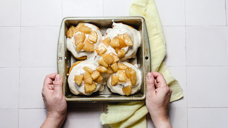 Hands holding a tray of cinnamon buns