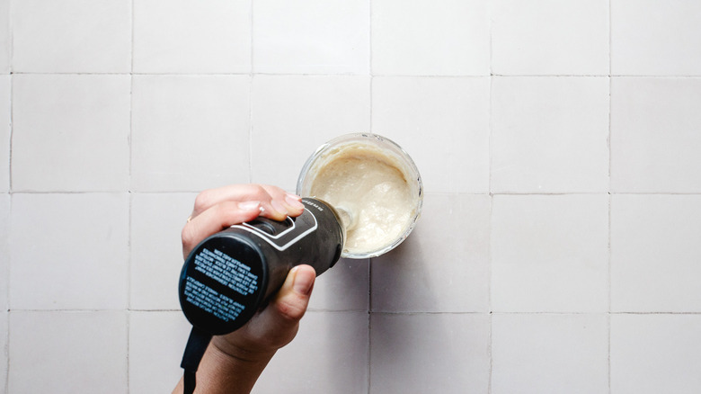 Hand holding an immersion blender in a jar of cream