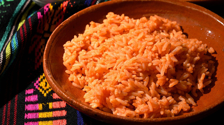 A bowl of Mexican rice beside multi-colored tablecloth