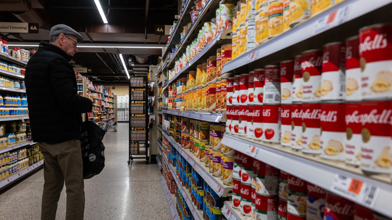 A customer looking at cans in the canned soup aisle of a grocery store