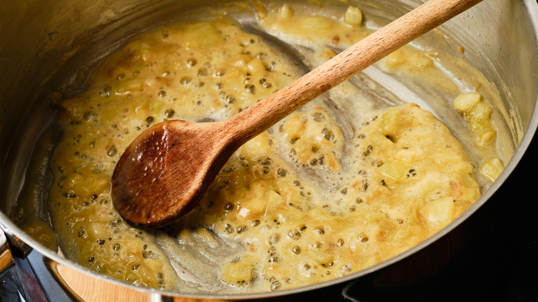 A bubbling Roux with onion in the bottom of a pot along with a wooden spoon
