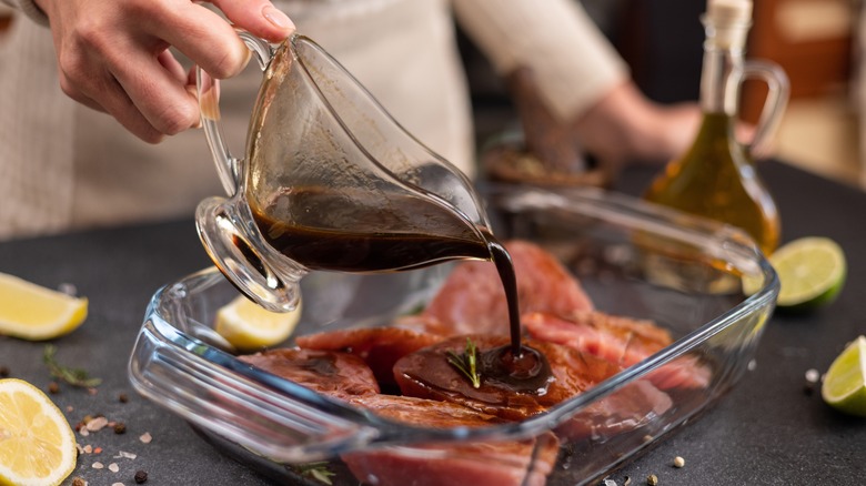 person pouring marinade over meat in a glass dish