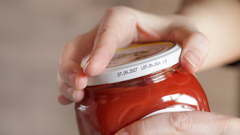 a person attempting to unscrew the top of a jar filled with thick red liquid