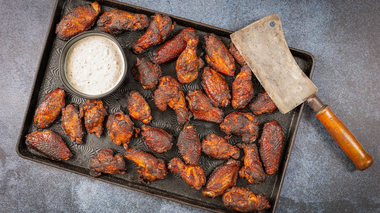 Tray of glazed chicken wings with sauce cup and meat cleaver