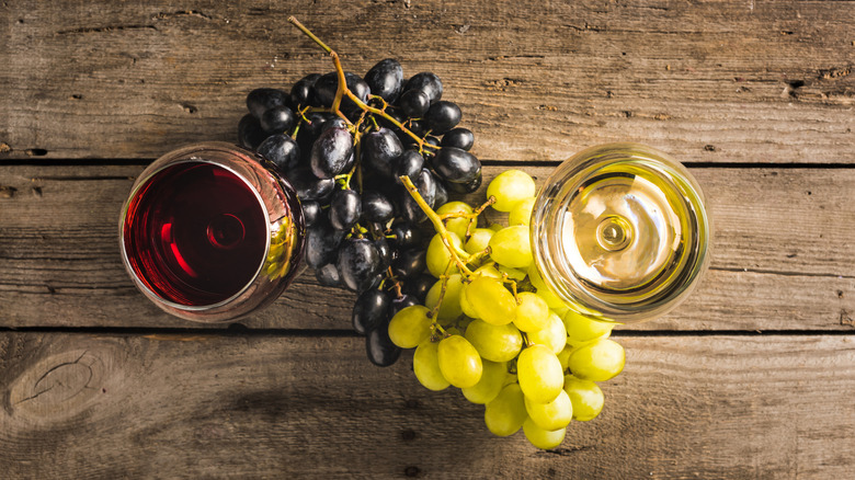 overhead photo of a glass of red wine and a glass of white wine with red and white grapes between them