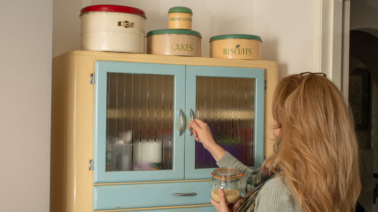 A woman reaching into a kitchen pantry that has frosted glass doors