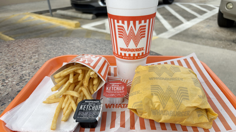 Whataburger meal tray with wrapped burger, ketchup packets, carboard container of fries, and soft drink cup