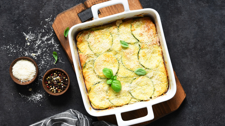 A square pan of zucchini casserole placed on a brown chopping board