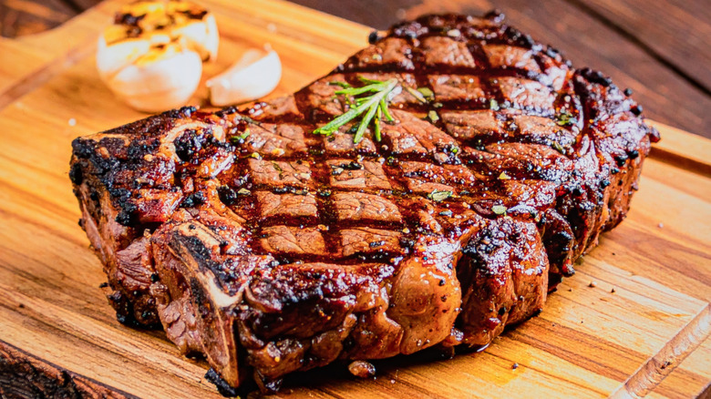 Grilled steak with char marks on wooden board with green herb garnish