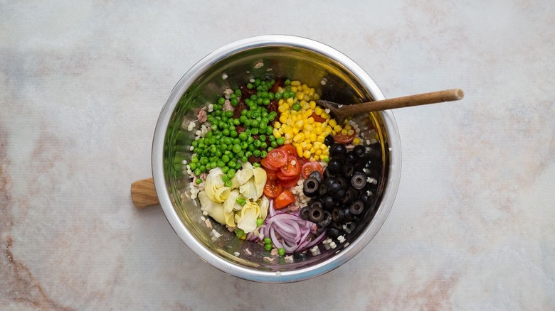 Peas, corn, olives, tomatoes, sliced onion, and artichoke hearts unmixed in bowl