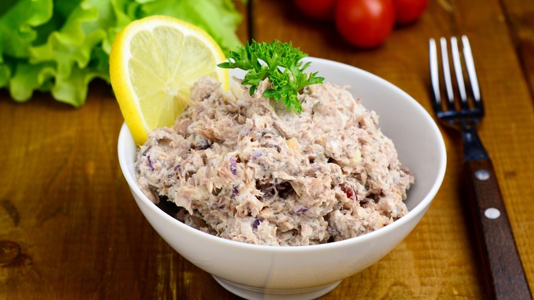 A simple bowl of tuna salad with a lemon slice and green garnish