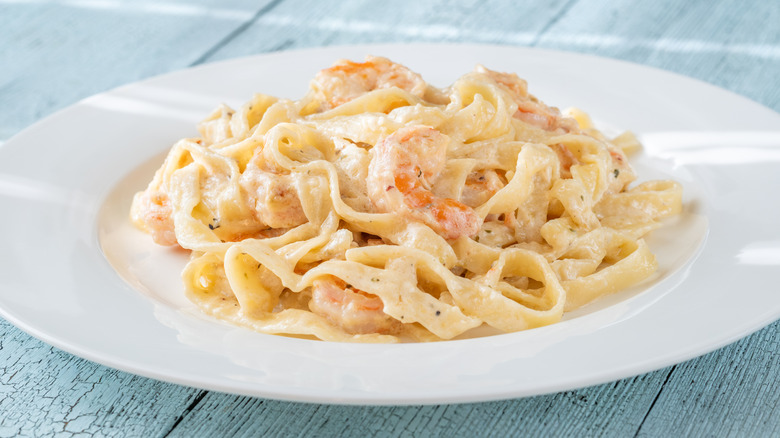 A white plate of a creamy seafood pasta for the visible black pepper and shrimp in the sauce