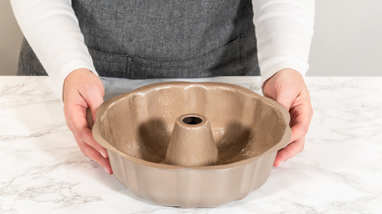 Hands holding a greased Bundt pan