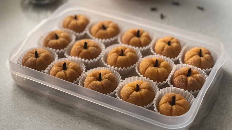 A rectangular container full of small brigadeiro candies shaped like pumpkins in small cupcake wrappers