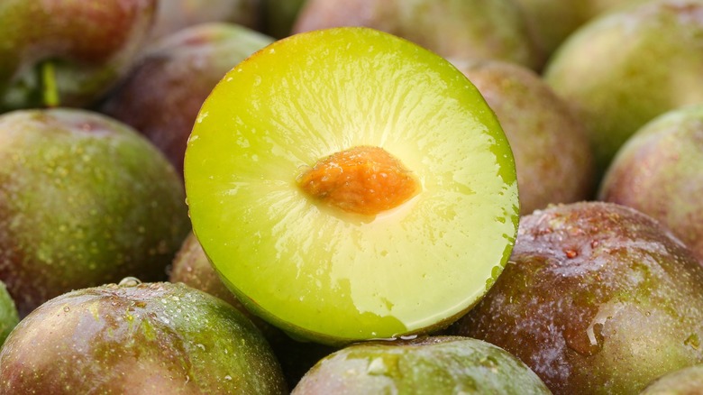 A plum that is cut in half exposing the pit inside sitting atop a pile of other plums