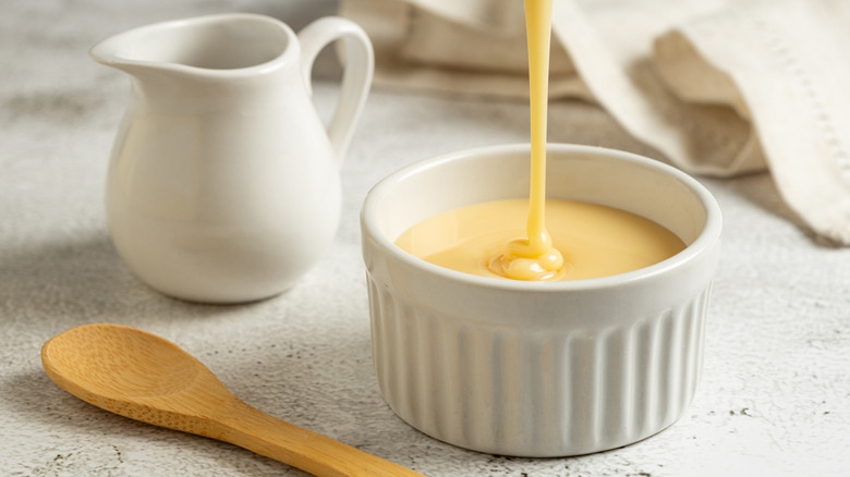 Condensed milk being poured into a ramekin next to small jug and spoon