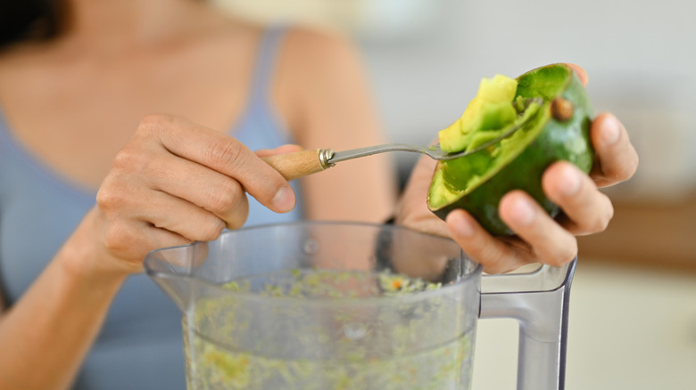 close up of woman adding avocado to blender