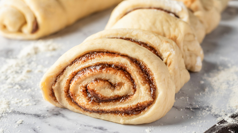 A roll of cinnamon roll dough sliced on a kitchen counter