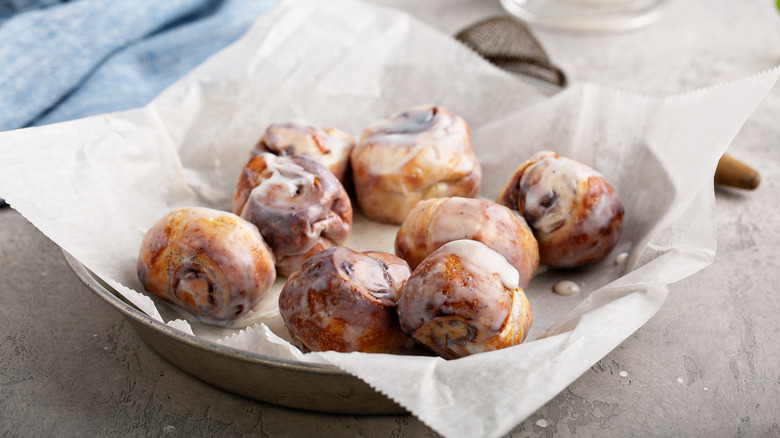 Glazed cinnamon roll bites on parchment paper in a baking pan