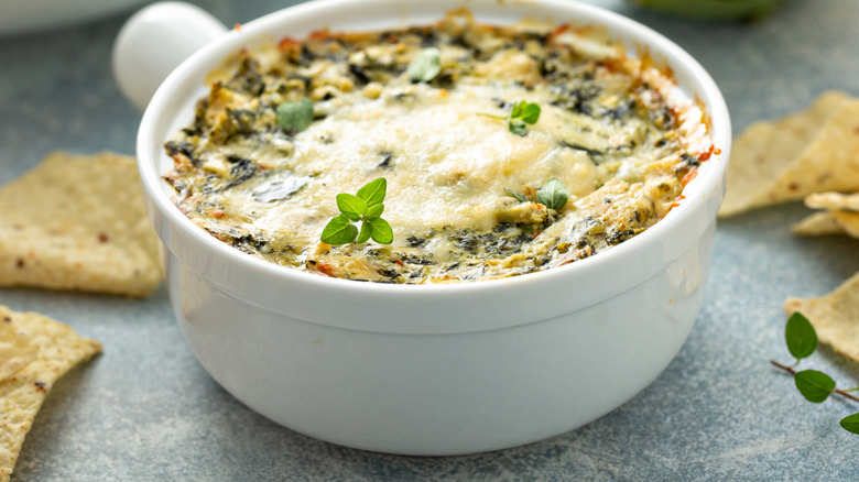 Baked cheesy dip with crispy cheesy topping and containing greens with tortilla chips on the side.