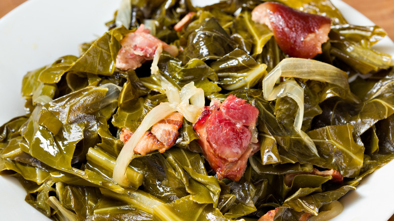 Cooked collard greens with pieces of meat on a white plate