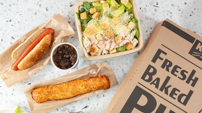 Costco food court items including a chicken Caesar salad, hot dog, pizza, and chicken bake