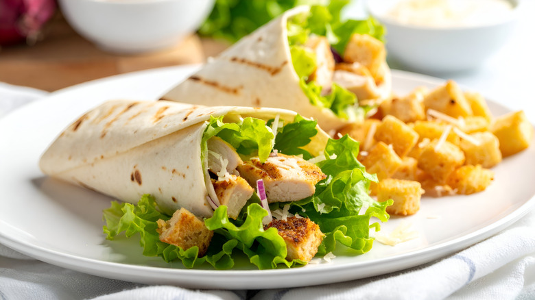 Two chicken Caesar salad wraps with croutons on a white plate