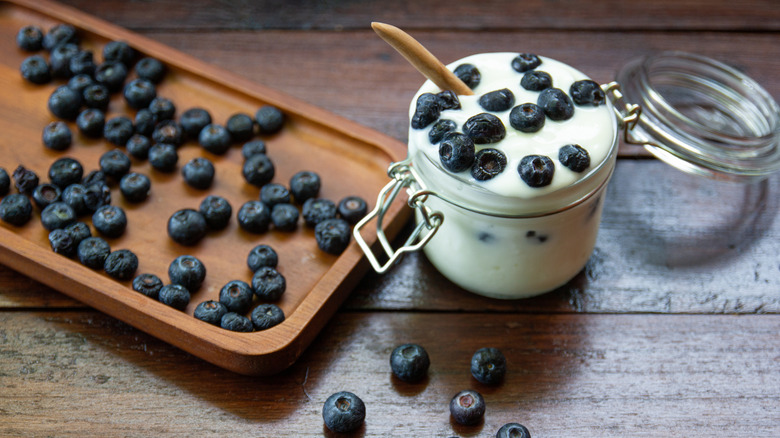 A jar of yogurt overflowing with blueberries next to a board filled with berries