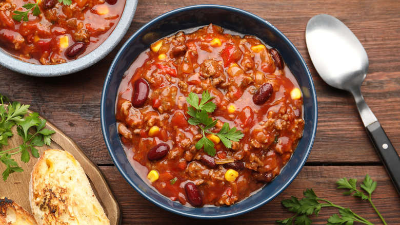 A bowl of chili on a wooden background, with a spoon on the side